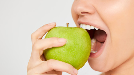 Woman with Apple. Beautiful girl closeup eating an apple on a gray background, healthy teeth. High...