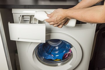 Close up view of male hand pouring detergents into washing machine.