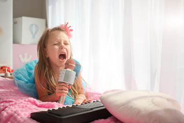  Beautiful little girl in a princess costume sings into a karaoke microphone.