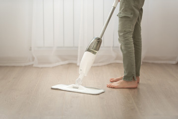 Fototapeta premium a child in green pants mops the floor in a bright apartment