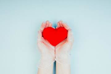 Obraz premium Female hands in medical gloves hold a red heart. Pandemic Health Care Concept for Doctors