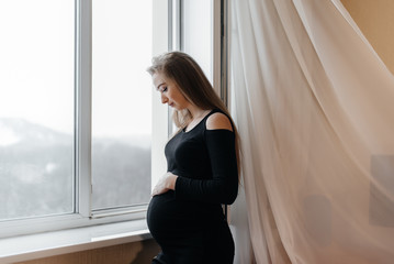 A pregnant girl is breathing fresh air from the window