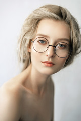 Fototapeta na wymiar Close-up portrait of a girl in round glasses. young woman with clean beautiful skin and juicy pink lips. beauty portrait of a blonde with blue eyes and light makeup