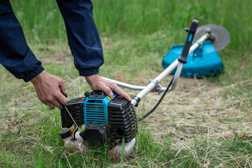 A man pulls on a winding cable, starts the engine of a gas trimmer