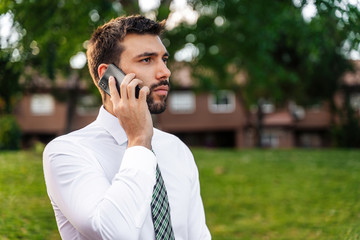 Young business man with white shirt and tie in outdoor park making phone call