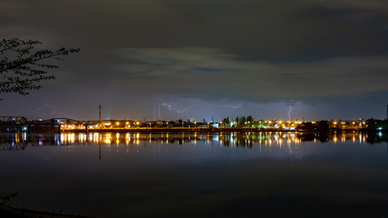 Night city during a thunderstorm on the horizon. River, sky, lightning over the city. Horizontal orientation.
