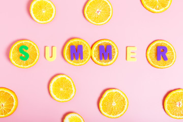  The word summer from multi-colored letters on slices of an orange on a pink background. Summer concept. Top view, flat lay.