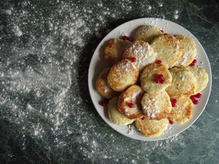 Cheesecakes on a plate, decorated with cranberries and icing sugar on top, on a background a green marble table and flour.