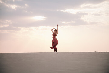 Fototapeta na wymiar Girl in red dress at sunset in the desert