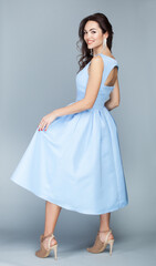 Portrait of beautiful young european brunette girl in light blue dress on grey background