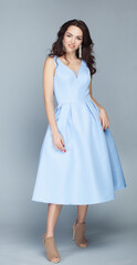 Portrait of beautiful young european brunette girl in light blue dress on grey background