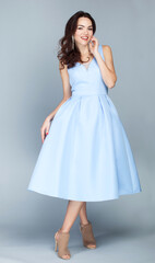 Portrait of beautiful young european brunette girl in light blue dress on grey background