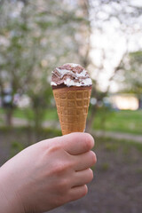 Woman's hand holding melting ice cream waffle cone on summer light nature background