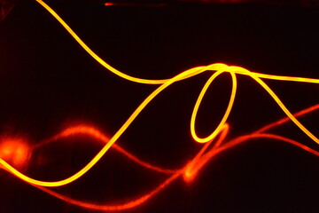A light guide, a wire with orange light, a light guide wire with different light transmission, light spectrum, and light effects located in a chaotic state with light reflection on a black glossy back