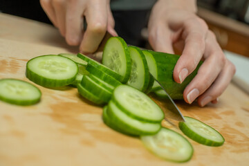 Women's hands cut a fresh cucumber into circles on a wooden Board close up