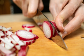 Women's hands cut radishes into circles with a knife on a wooden Board