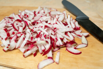 Sliced radishes for salad in close-up on a wooden Board next to a knife.
