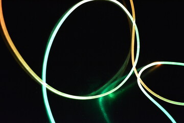 A wire with orange and green light, a light guide wire with different light transmission, light spectrum, and light effects located in a chaotic state with light reflection on a black glossy backgroun