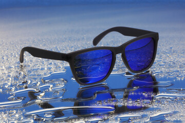 Blue sunglasses with black frames on water reflection with selective focus