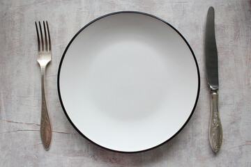 Empty white plate with silverware knife and fork on a light background. View from above.