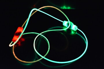 Wire with green and red light, a light guide wire with different light transmission, light spectrum, and light effects located in a chaotic state with light reflection on a black glossy backgroun