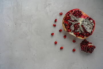 Half of pomegranate and pomegranate seeds are laying at the right side on concrete surface
