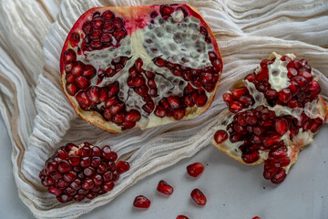 Half of pomegranate and pomegranate slices are laying on beige textile