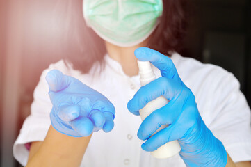 The concept of protection against bacteria and viruses. Woman wearing surgical face mask and gloves,protective against influenza sickness, holding white spray bottle with alcohol for disinfection