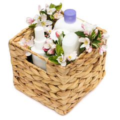 White cosmetic bottles in a wicker basket with pear flowers isolated on a white background. Natural organic cosmetics concept.