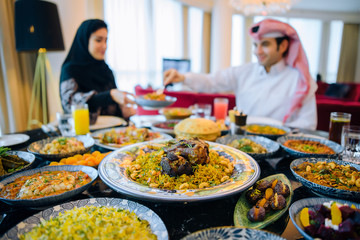 Arab family in traditional clothes eating during the holy month of Ramadan at Iftar. Feast in honor of Eid Mubarak. The family sits on the background of a table filled with traditional food