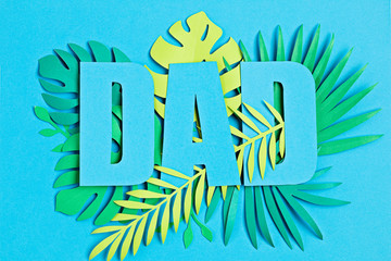 Fototapeta na wymiar Fathers Day. Word Dad over paper cut tropical leaves and blue background. Greeting card