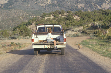 A boy in the back of a pickup truck chasing a dog in the NM desert © spiritofamerica