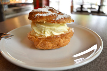 Pie Eclair with whipped cream and powdered sugar on a white plate.