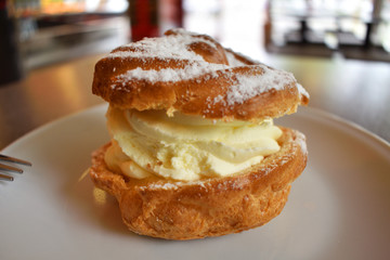 Pie Eclair with whipped cream and powdered sugar on a white plate.