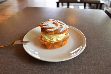 Pie Eclair with whipped cream and powdered sugar on a white plate.