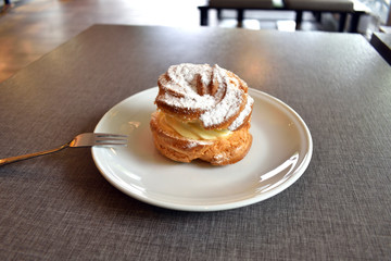 Pie Eclair with whipped cream and powdered sugar on a white plate.