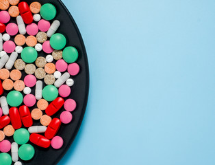 Different colorful pills on black plate, blue background.