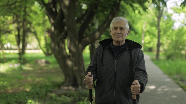 Active senior old man training Nordic walking with ski trekking poles in park