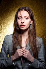Portrait of sensual brunette with wet hair, wear grey jacket. Gold background. Elegance makeup.