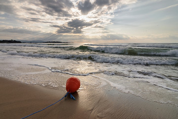 Red floating buoy lies on the sand of the Black Sea. Landscape with beautiful sky