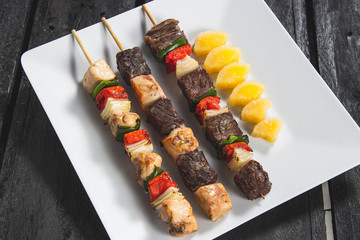 Espetinhos assados de carne, frango com legumes, carne com legumes e mandioca cozida servido em prato no boteco