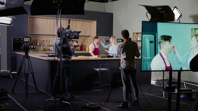 WIDE Behind the scenes of studio set, makeup artist make corrections during shooting television cooking show featuring celebrity chef, professional TV production. Shot on ARRI Alexa Mini