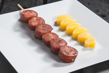 Espetinho assado de linguiça calabresa com mandioca cozida servido em prato no boteco
