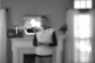 Drone flying indoors with pilot visible in background. Amateur drone flight. User wearing sweatshirt flying drone inside of home on cold day. White drone flying inside.