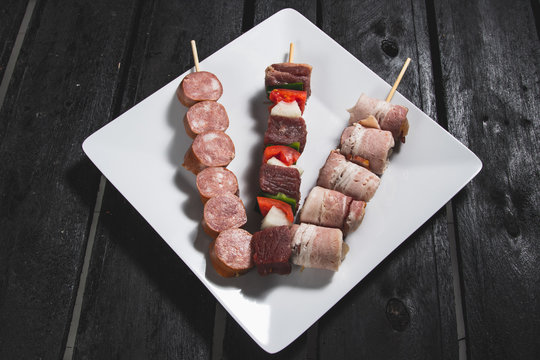Espetinhos crus de carne com legumes, lingui&ccedil;a calabresa e medalh&atilde;o de frango ou carne servido em prato no boteco