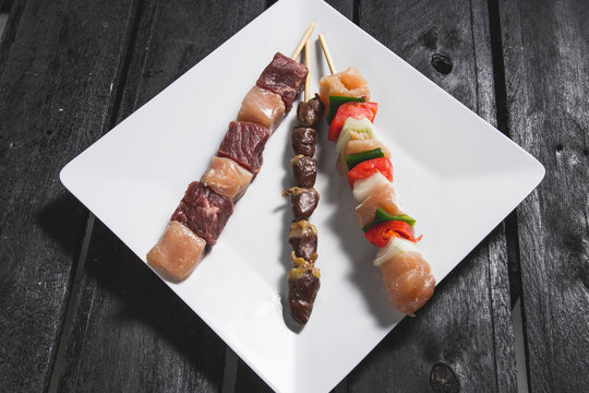 Espetinhos crus de carne, cora&ccedil;&atilde;o de frango e frango com legumes servido em prato no boteco