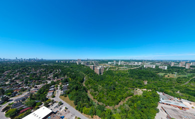 Sunny summer day with plain blue sky and panoramic city landscape in Toronto, Ontario, Canada from urban industrial area to the residencies. Factories, houses, stores, parks, roads with green trees.