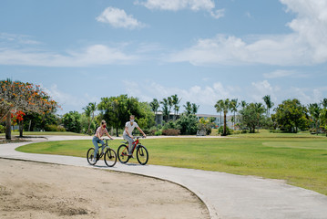 Fototapeta na wymiar 2 cyclists (woman and man) ride a bike in the park. They wear protective masks against coronavirus covid-19