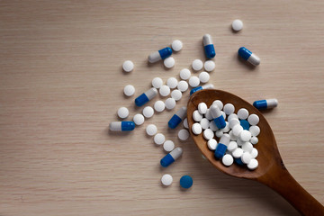 Fototapeta na wymiar Assorted pharmaceutical white and blue medicine tablets, tablets and capsules on a wooden spoon