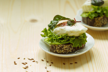 Poached egg on grain bread with green lettuce leaves close up